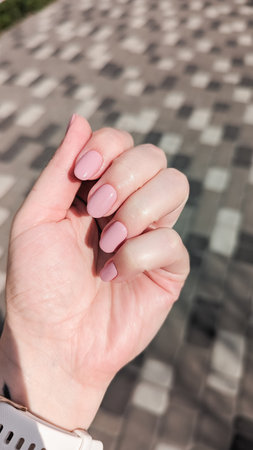 Manicured hand showing shiny pink nail polish against patterned background.の写真素材