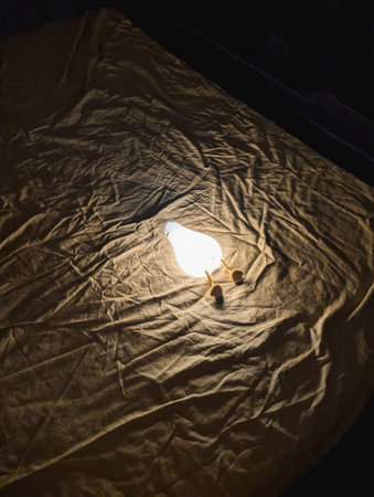 Illuminated lamp on textured fabric background, dim lighting. Soft shadow and warm glow.の写真素材
