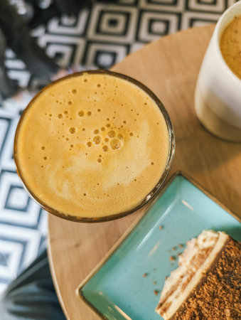 Frothy coffee in glass with dessert on wooden table. Cozy cafe ambiance.の写真素材