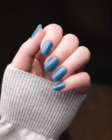 Female hand with trendy blue glitter striped nail polish manicure. Beautiful nail art design with sparkling effect. Modern beauty trend, elegant style.