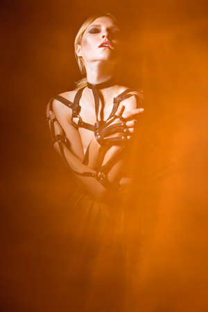 Beautiful fashionable woman in a leather sword belt and fire around. Art image. Picture taken in the studio with mixed light.の写真素材