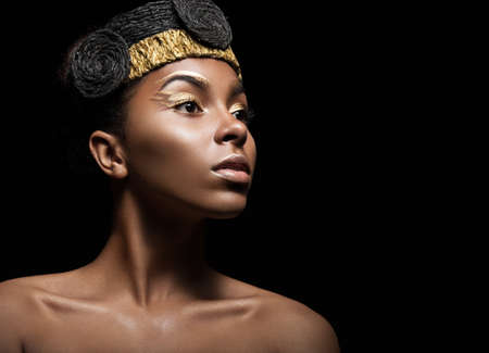 African girl with bright makeup and creative gold accessories on the head. Beauty face. Picture taken in the studio on a black background.の写真素材