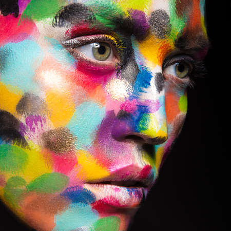 Girl with colored face painted. Art beauty image. Picture taken in the studio on a black background.の写真素材
