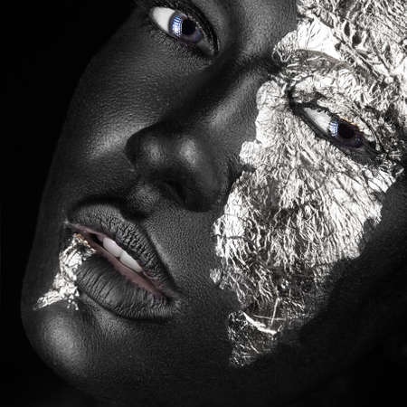 fashion portrait of a dark-skinned girl with silver foil make-up.Beauty face. Picture taken in the studio on a black background.の写真素材