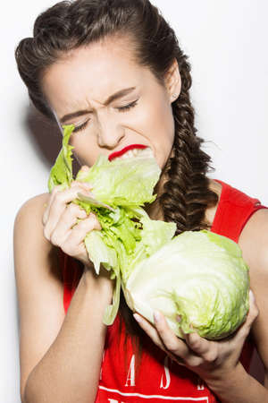 Daring funny girl with braids and red lips, emotional eating cabbage. Beauty emotion face. Picture taken in the studio on a white background.の写真素材