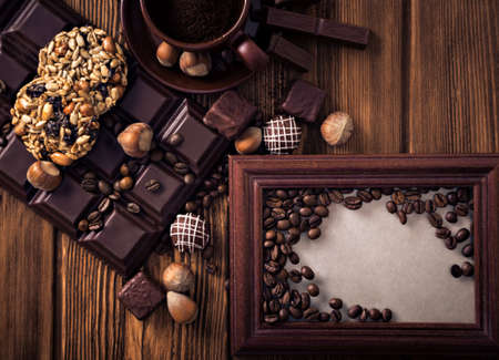 Roasted coffee beans, chocolate, candy, nuts, and a cup with ground coffee and the frame for the inscriptions on the wooden background.の写真素材