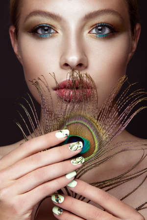Beautiful girl with bright makeup, manicure design and peacock feather on her face. Art nails. Photos shot in the studio.の写真素材