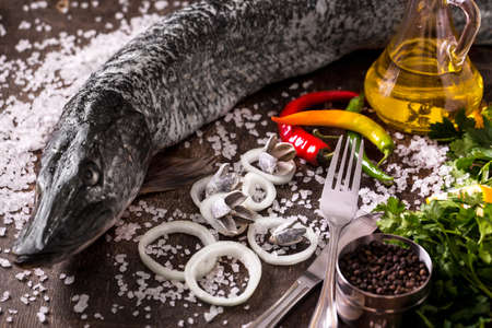 Delicious fresh fish on dark vintage background. Fish with aromatic herbs, spices and vegetables -...