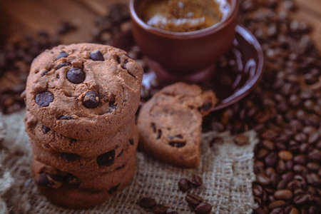 Roasted coffee beans, biscuit with chocolate and cup on the wooden background.