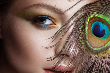 Beautiful girl with bright colored makeup and peacock feather on her face. Beauty face. Close-up. Photos shot in the studio.の写真素材