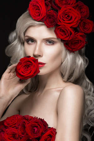 Beautiful blond girl in a dress and hat with roses, classic makeup, curls and red lips. Beauty face. Photos shot in studioの写真素材