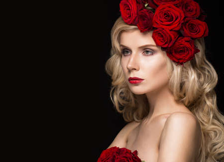 Beautiful blond girl in a dress and hat with roses, classic makeup, curls and red lips. Beauty face. Photos shot in studioの写真素材