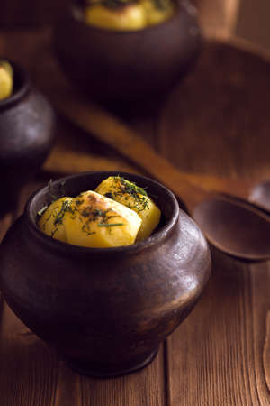 Baked potato in old pot on wooden background with pickled cabbage and cucumber.の写真素材