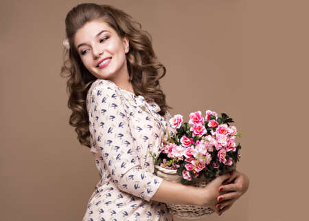 Fresh young girl in a light silk dress, smile, retro curls in the style of pin-up with a basket of flowers in her hands. Beauty face and body. Photos shot in studioの写真素材
