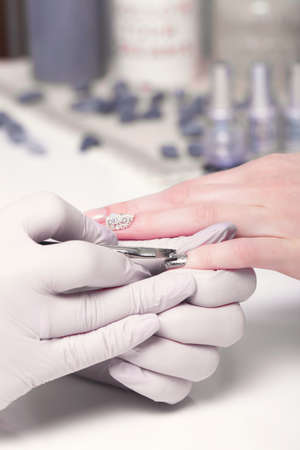Closeup finger nail care by manicure specialist in beauty salon. Manicurist paints nails with nail...