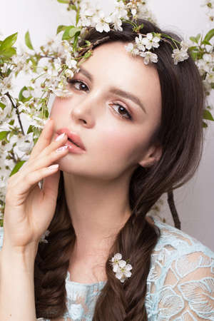 Beautiful brunette girl in blue dress with a gentle romantic make-up, pink lips and flowers. The beauty of the face. Portrait shot in the studio.の写真素材