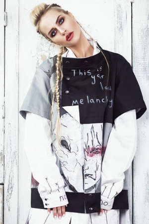 Creative unusual blond girl in designer clothes and braids on her head posing in the studio.