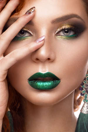 Beautiful redhair model: curls, bright makeup, jewelry and green lips. The beauty face. Portrait shot in the studio on a brown background.の写真素材