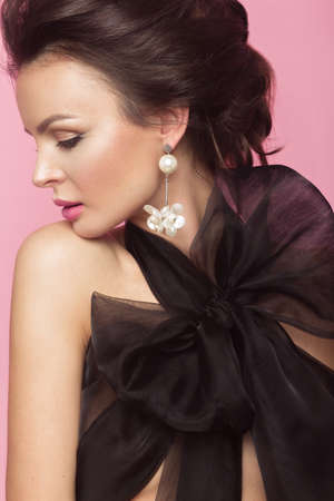 Fashion beautiful woman in black dress with bow, retro make-up and hair. Beauty face and body. Photo taken in studio on a pink backgroundの写真素材
