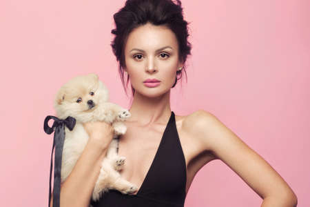 Fashion beautiful woman in black dress with bow, retro make-up and hair. Beauty face and body. Photo taken in studio on a pink backgroundの写真素材