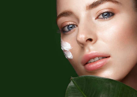 Beautiful fresh girl with cosmetic cream on the face, natural make-up and green leaves. Beauty face....