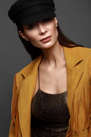 Beautiful girl with a classic make-up and a hairstyle in a fashionable designer jacket and cap, posing in the studio. Beauty faceの写真素材