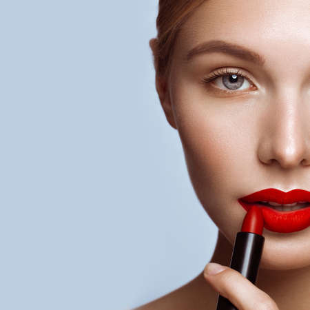 Beautiful girl with red lips and classic makeup with lipstick in hand. Beauty face. Photo taken in the studio.の写真素材