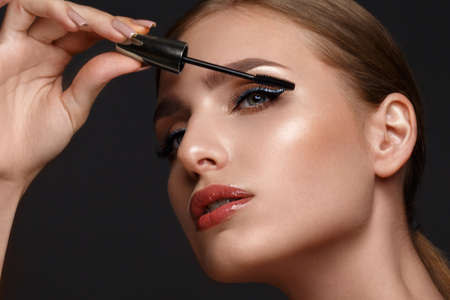 Beautiful girl with sexy lips and classic makeup with cosmetic mascara brush in hand. Beauty face....
