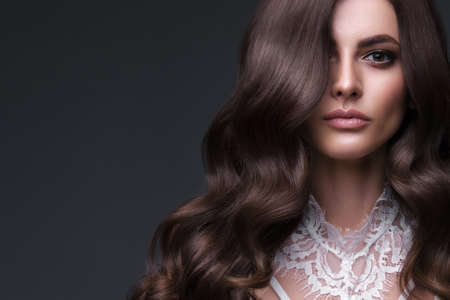 Beautiful brown-haired girl with a perfectly curls hair, and classic make-up. Beauty face and hair.の写真素材