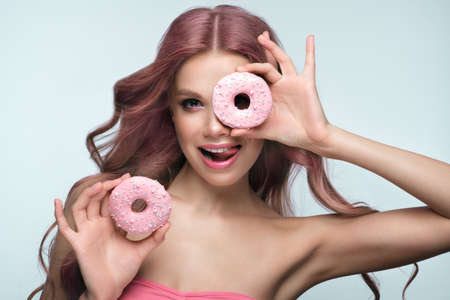 Beautiful woman with pink hair, beautiful makeup with donuts in her hands posing in the studio.の写真素材