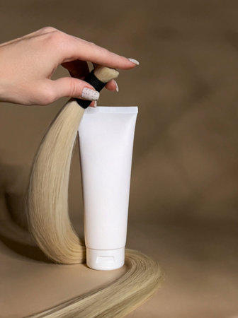 A strand of natural light hair for extensions with a bottle of care product.の写真素材