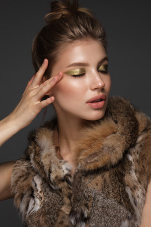 Portrait of a beautiful woman in a furcoat with creative gold makeup in a fashion style. Beauty face.の写真素材