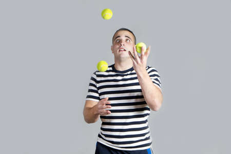 Young juggling tennis balls on grey backgroundの写真素材
