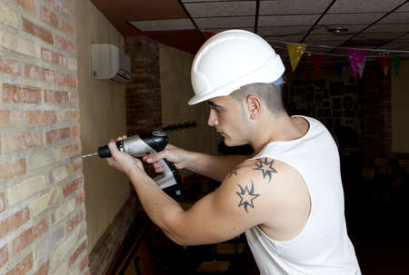 young worker making a hole in the wall with a drillのeditorial素材