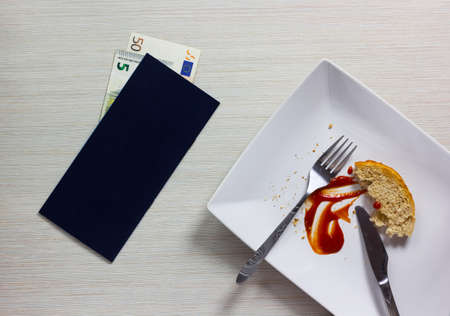 Empty plate left after dinner with bill and Euro note on wooden tableの写真素材