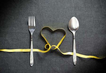 Fork and spoon with heart shape made from yellow ribbon on black textured backgroundの写真素材