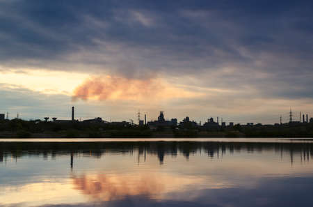 Chimney smoldering mirroring in water with rain cloudsの写真素材