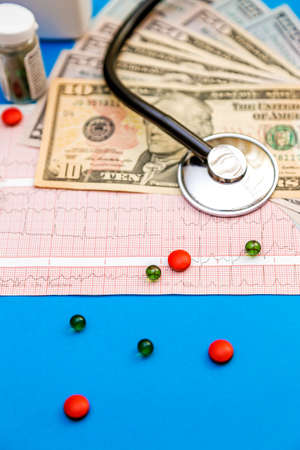Stethoscope on cardiogram sheet with dollar bills and pills on blue backgroundの写真素材