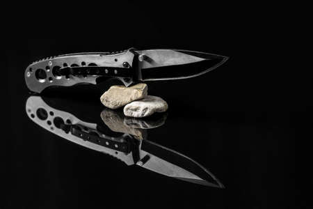 Folding hunting knife on stones mirroring on black background.Useful for adventure, military, hunting, outdoor, protection, security, background presentationの写真素材