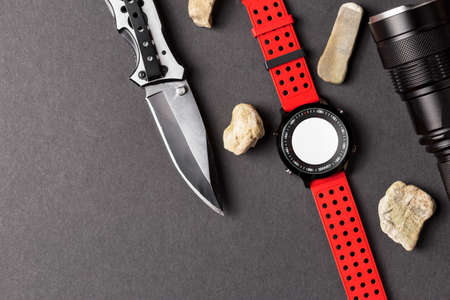 Hunting objects, folding hunting knife, red smartwatch and black flashlight on black background, Useful for adventure, military, hunting, outdoor, protection, security, background presentationの写真素材