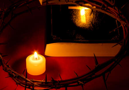 Crown of Thorns of Jesus Christ put on the Bible beside a candle on a red background.の写真素材