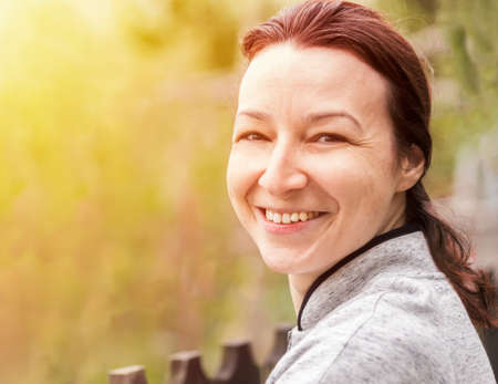 Happy young woman with natural skin in nature. Portrait of woman with natural skin, no makeup, looking at the cameraの写真素材