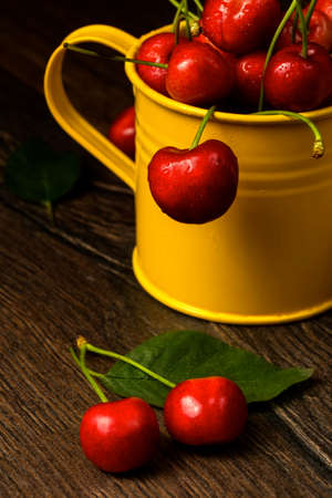Cherry berries in yellow bucket container on wood table background.