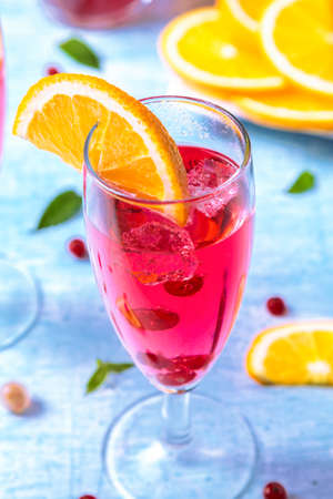 Refreshing summer drink with sliced orange, red currant, mint leaf over blue background
