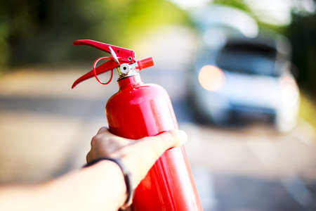 Man with a fire extinguisher in his hand. The concept of helping cars in flame.の写真素材