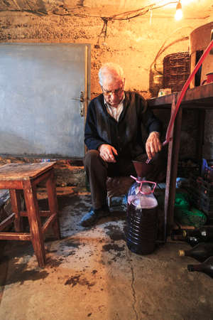 Old man stands in the old wine cellar and extracts the wine in bottles