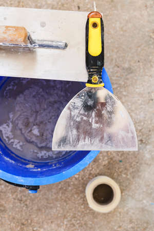 Bucket with plaster and metal building spatula. Above view and close up.