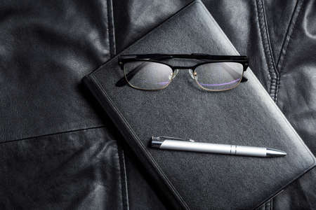 Notebook, glasses and pix over black leather background. Business minimalist lifestile presentation background.の写真素材
