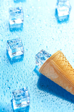 Ice cream cone and melted ice cubes on fresh blue background