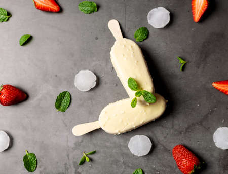 Ice cream strawberry stick covered with white chocolate, popsicle , on black marble table, flat lay